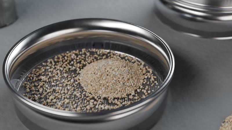 Stainless steel test sieve with sand grains retained on the wire mesh, further sieves in the background